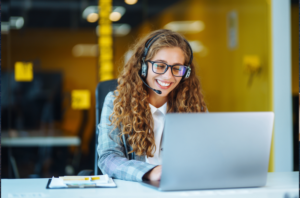 A smiling delivery coordinator sitting with a laptop and communication headset