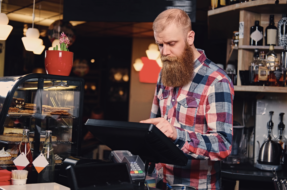 A bearded restaurant worker tapping a countertop order system tablet screen